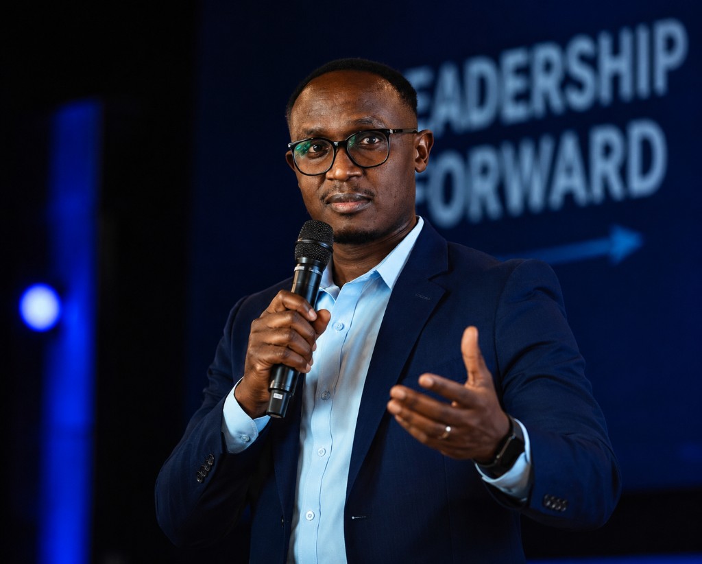 Dr. Kevin Muchiri speaking on stage with a microphone at a Leadership Forward event